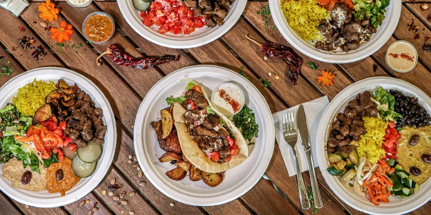 Plated Mediterranean kebab meals with rice, vegetables, and dips on wooden table
